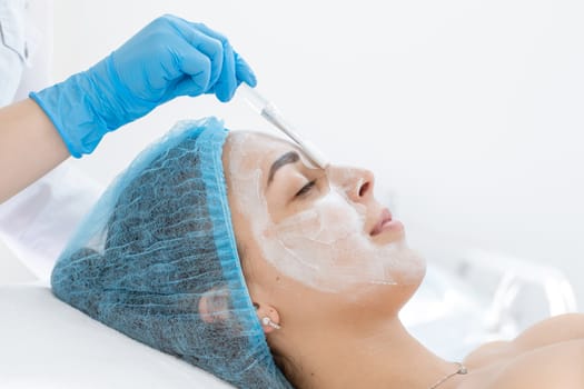 Woman professional doctor beautician applies a mask on a patient's face for skin care. Cosmetic procedures for skin rejuvenation and nutrition.