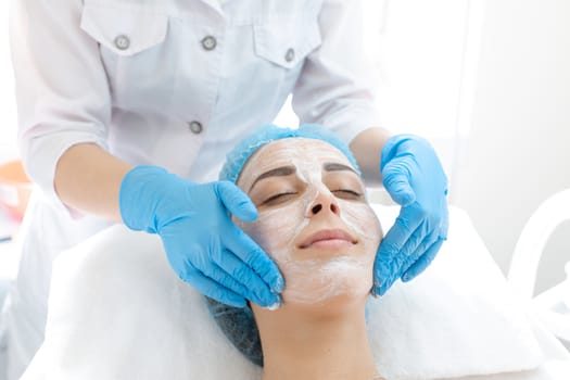 Woman professional doctor beautician applies a mask on a patient's face for skin care. Cosmetic procedures for skin rejuvenation and nutrition.