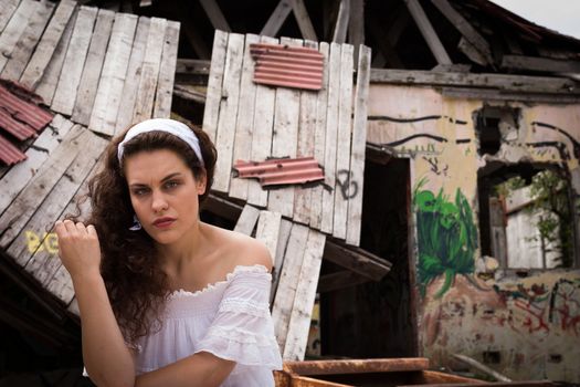 Beautiful young woman in light dress sitting in front of the ruins of a ghost town