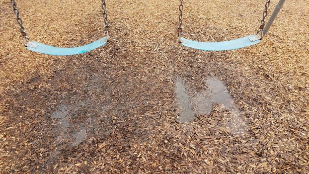 blue seat on swing with water puddle and wet mulch