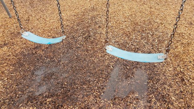 blue seat on swing with water puddle and wet mulch