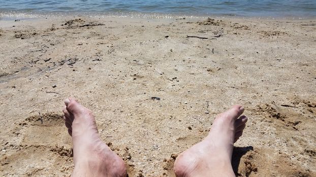 male feet on sand and pebbles at beach or coast with water