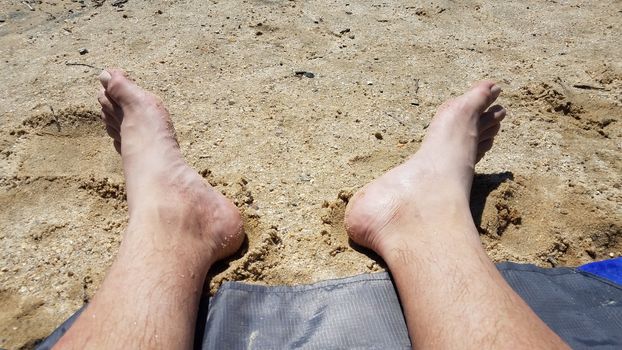 male feet on sand and pebbles at beach or coast