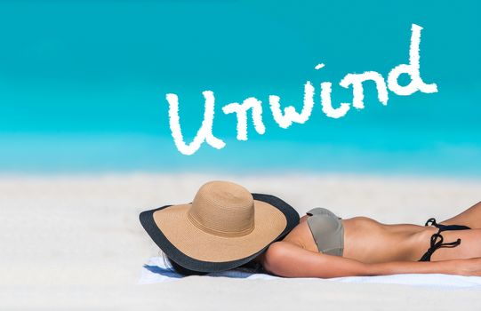 UNWIND word written on sky above beach travel bikini suntan woman sleeping relaxing covering face with hat doing siesta. UNWIND text in blue ocean copyspace above. Summer and sun vacation holidays.