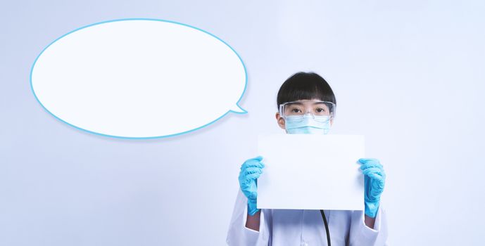 Asian woman doctor holding a blank paper in hand and copy space and she wear medical glove and face mask and doctor suit for protect virus pandemic. studio shot on plain background.