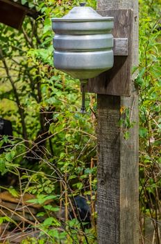 an old manual aluminum washbasin tank hangs on a wooden bar in the garden of a suburban plot