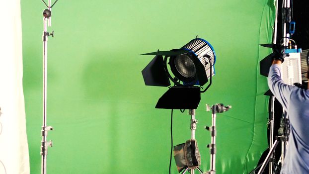 Big studio LED spotlight for video movie or photo film production with green screen background for chroma key technique in post lab process and professional equipment such as tripod and others.