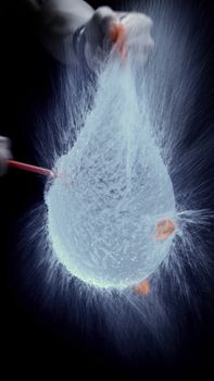 Water balloon exploding or splashing which represent power of refreshing or freshness for viewer and blasted by pencil in hand on black background in the studio.