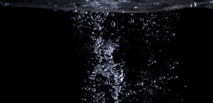 Blurry images of clear transperant soda liquid bubbles splashing or sparkling and moving up in black background for represent the refreshing moments after drink carbonated water.