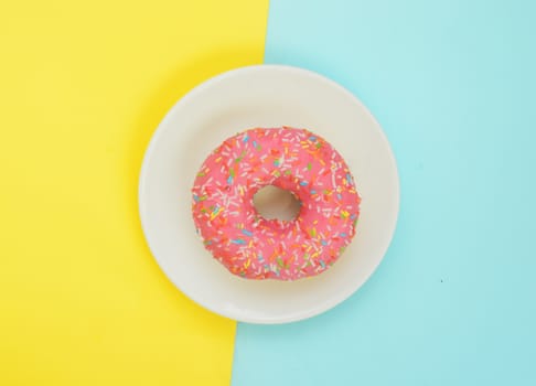 Top view,One pink glazed donut on white plate on pastel yellow turquoise background.Sweet dessert for snack.