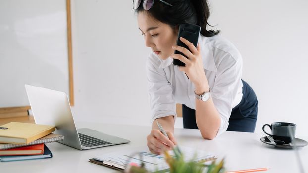Young female entrepreneur working laptop computer and talking mobile phone.