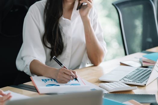 Young accountant hand holding smartphone to call marketing consultants and using laptop computer to analyze sales growth in the global workplace market. accounting concept.