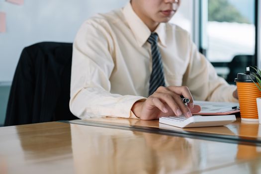 Close up of businessman or accountant hand holding pen working on calculator to calculate business data, accountancy document and laptop computer at office, business concept.