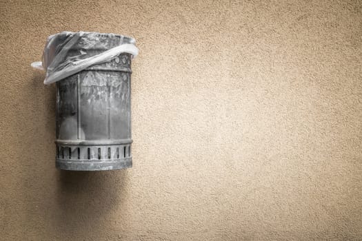A municipal garbage basket, hanging from a wall.