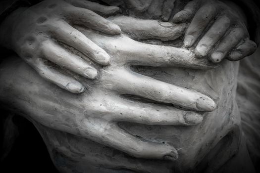 Detail of a marble statue with hands of child and woman together.