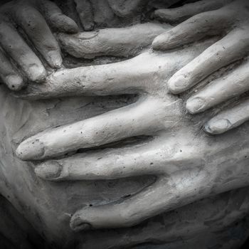 Detail of a marble statue with hands of child and woman together.