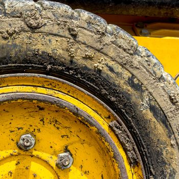 Extreme close up of tire bulldozer, yellow and covered with mud.