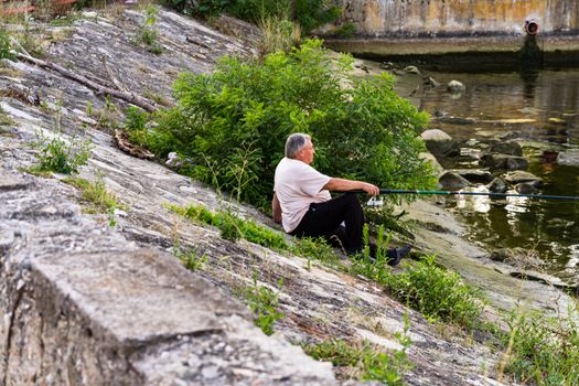 Man relaxing and fishing from the edge of a river in Orsova, Romania, 2020