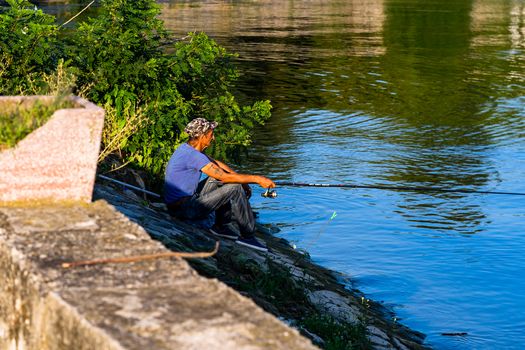 Man relaxing and fishing from the edge of a river in Orsova, Romania, 2020