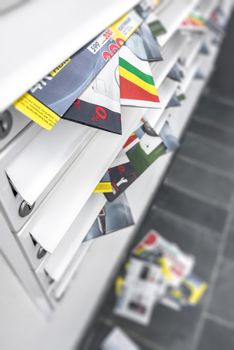 Modern metal mail boxes, overfull of leaflets; some have fallen on the ground. Ideal for concepts. Shallow depth of field.