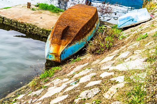 Old and rusty iron overturned boat on the shore, on the edge of a river.