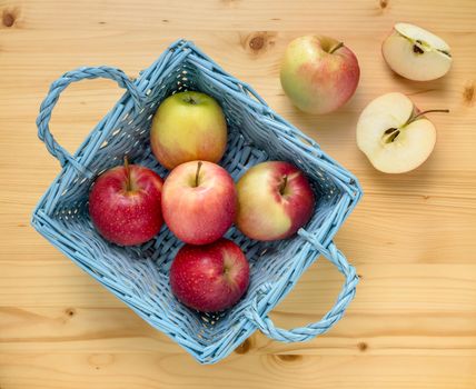 Red apples in blue wooden basket on wooden table. Two apples are remained out of the basket and one is cut. Top view.