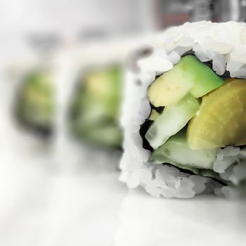 Vegan sushi roll with rice and avocado. Defocused blurry background.