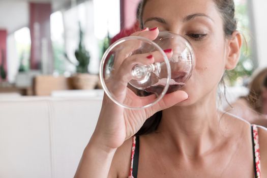 Closeup portrait of young woman with ponytail drinking red wine. Leisure, drinks, degustation, people and holidays concept. Defocused blurry background.