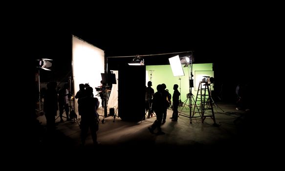 Silhouette images of video production behind the scenes or b-roll or making of TV commercial movie that film crew team lightman and cameraman working together with director in big studio with professional equipments 