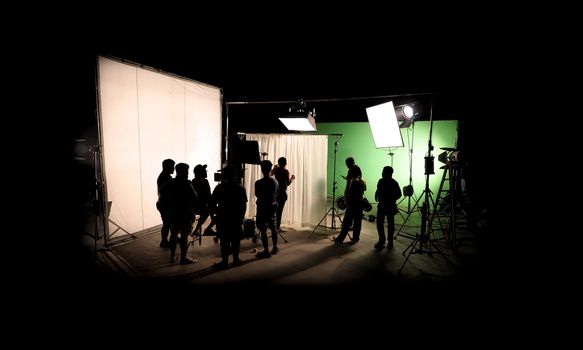 Silhouette images of video production behind the scenes or b-roll or making of TV commercial movie that film crew team lightman and cameraman working together with director in big studio with professional equipments 