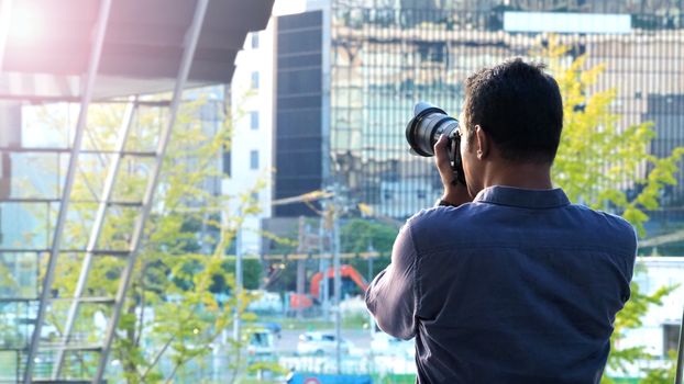 Behind tourist or traveller standing taking a photo of tower in Osaka Japan near station around Umeda area by dslr camera in hands and have a sunset flare in the evening day.