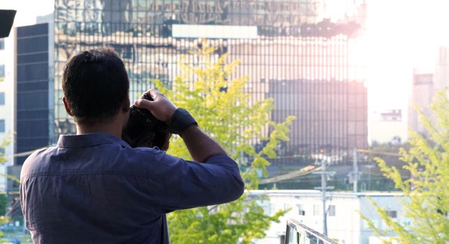 Behind tourist or traveller standing taking a photo of tower in Osaka Japan near station around Umeda area by dslr camera in hands and have a sunset flare in the evening day.