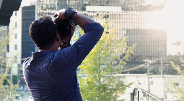 Behind tourist or traveller standing taking a photo of tower in Osaka Japan near station around Umeda area by dslr camera in hands and have a sunset flare in the evening day.