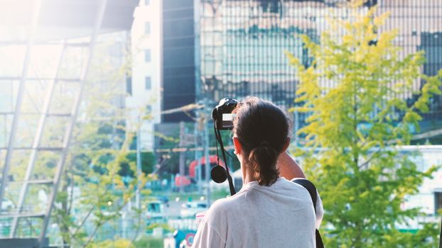 Behind tourist or traveller standing taking a photo of tower in Osaka Japan near station around Umeda area by dslr camera in hands and have a sunset flare in the evening day.