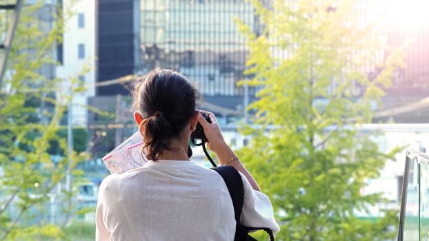 Behind tourist or traveller standing taking a photo of tower in Osaka Japan near station around Umeda area by dslr camera in hands and have a sunset flare in the evening day.