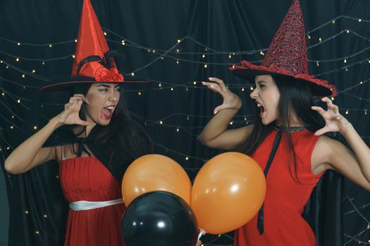 Beautiful woman and friend in Halloween devil costume and wearing witch hat. Have fun at nightclub party, decorate the lights by doing a scary face. Halloween celebration