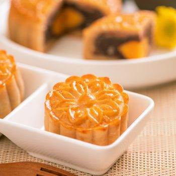 Tasty baked egg yolk pastry moon cake for Mid-Autumn Festival on bright wooden table background. Chinese festive food concept, close up, copy space.