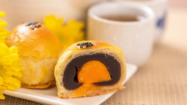 Tasty baked egg yolk pastry moon cake for Mid-Autumn Festival on bright wooden table background. Chinese festive food concept, close up, copy space.