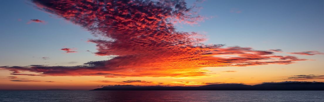 Beautiful panorama of clouds at sunset above the English Channel. Orange, red and purple colors in the blue sky. Golden hour landscape.
