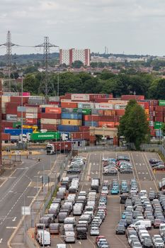 Southampton port, England, UK - June 08, 2020: Parking lot full of cars in the port of Southampton. Shipping containers in the background.