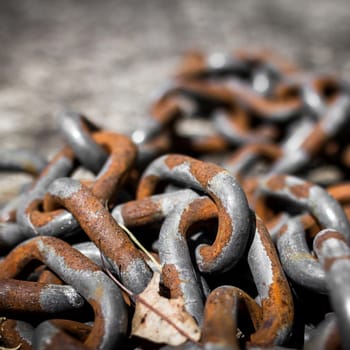 Closeup of a pile of thick rusted chains in sunlight. (Shallow DOF).