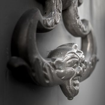 Traditional italian style metal knocker on the door. Extrem close-up. Defocused blurry background.