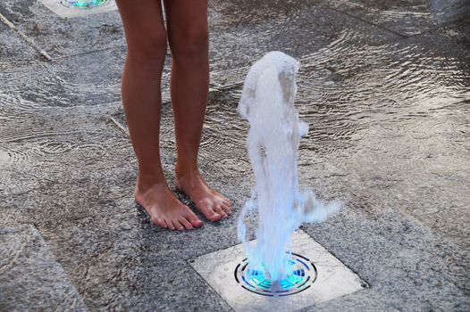 barefoot girl touching the fountain on the sidewalk in the evening.