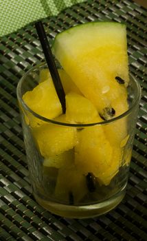 Yellow watermelon in a glass with slices and wedges with a straw