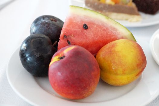 fruits - plums, peaches and watermelon on a plate close up