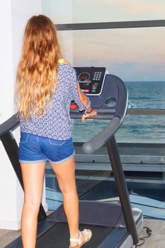 tteenage girl on a treadmill in the gym in front of the window with a sea view, back view.