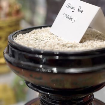 Uncooked sticky rice in oriental bowl. Extreme selective focus. Defocused blurry background.