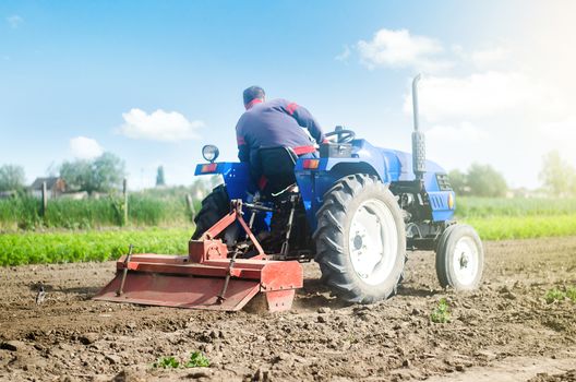 Farmer on a tractor with a milling machine processes loosens soil in the farm field. Preparation for new crop planting. Loosening surface, cultivating the land. Grind and mix soil on plantation.