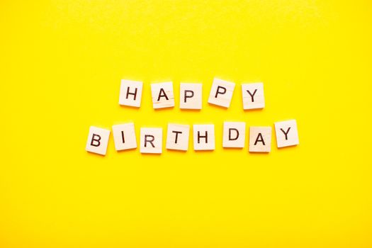 The inscription happy birthday made of wooden blocks on a light yellow background.
