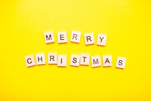 The inscription merry christmas made of wooden blocks on a light yellow background.